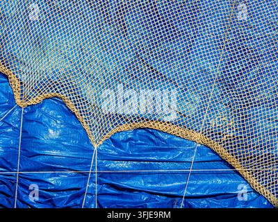 Fishing net creating a grid pattern over a wrinkled blue tarp Stock Photo