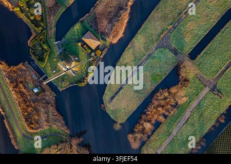 Rietveldse windmill is a historic polder mill controlling water levels in green agricultural fields and navigating canals under a clear sky, showcasing traditional Dutch landscape Stock Photo