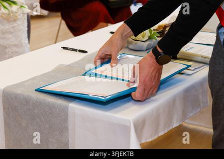 Person signing a document on a table covered with white and gray cloth. Stock Photo