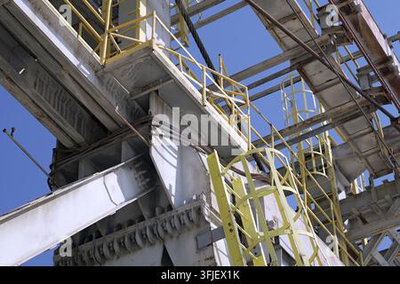 Large industrial metal structure details fill the frame, showcasing sturdy beams, platforms, and ladders, all set against a vibrant clear blue sky, il Stock Photo