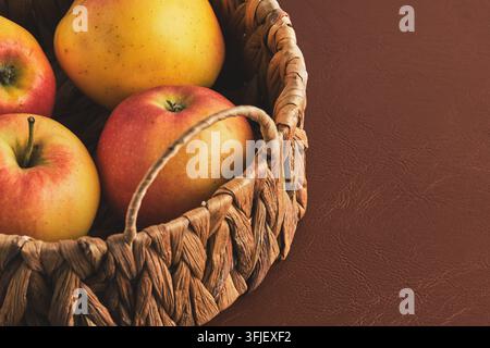 Fresh ripe apples in woven basket on brown leather surface, close up view Stock Photo