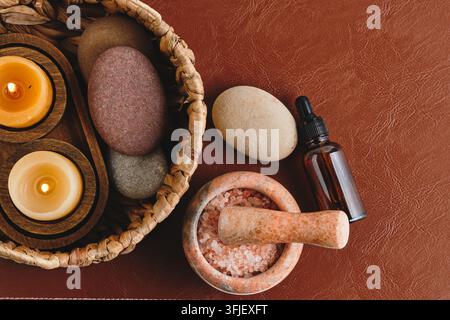 Spa and wellness items including candles in basket, stones, oil and salt mortar on table Stock Photo