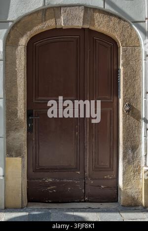 An old wooden double door stands beneath a rustic stone arch on a building facade. Stock Photo