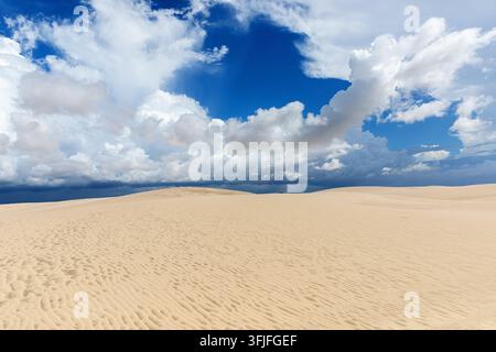 A dramatic view of vast white sand dunes stretching into the horizon under a dark, tempestuous stormy sky in Lencois Maranhenses, Brazil. Stock Photo