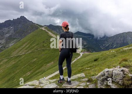 Female hiker with backpack standing on rocky mountain peak looking at Tatra range Stock Photo