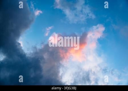 Pink and grey clouds float in a bright blue sky during sunset. Evening light, natural background, peaceful atmosphere. High quality photo Stock Photo