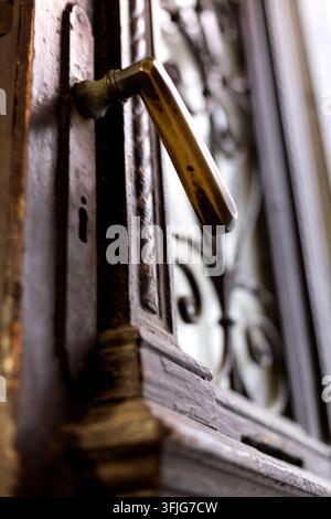 Close-up view of a worn brass door handle mounted on a weathered wooden door beside decorative metalwork. Soft natural light and shallow depth of fiel Stock Photo