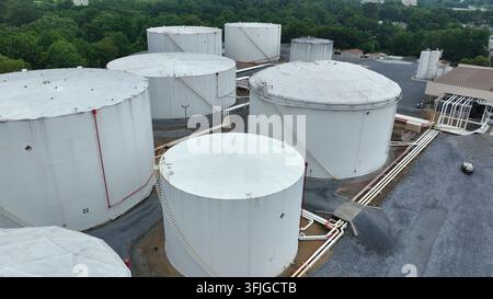 White rusty storage tanks for fuel at terminal in American town. Pipelines connecting circular silos. Aerial flyover shot. Industrial factory in Harri Stock Photo
