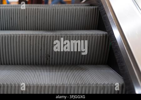 Detailed view of moving escalator stair treads showing characteristic parallel ribbed grooves and dirt accumulation in grooves, with stainless steel s Stock Photo