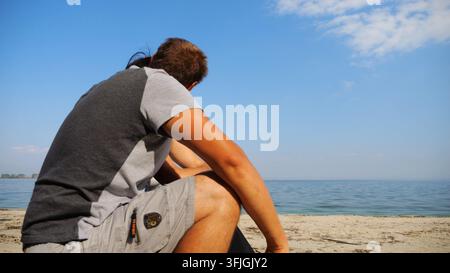 Happy couple hugs during sitting on wooden log on sandy beach. Romantic man kissing his beloved near coastline. Carefree lovers spending time together Stock Photo