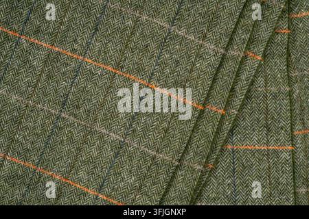Detailed close-up of textured green-gray woven fabric featuring a fine herringbone pattern with orange and blue accent lines. Stock Photo