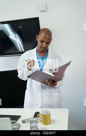 Medical professional reviewing a patient's bone x-ray and clinical documentation for diagnosis Stock Photo