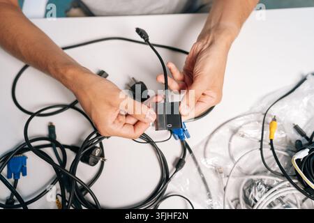 Close-up top view of person dealing with electronic clutter, organizing technology equipment. Concept of setting up new devices, repair, tech support Stock Photo