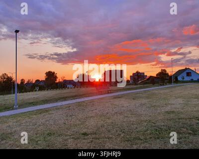 A scenic sunset view over a suburban residential area captured in late evening. The sky displays vibrant hues of orange, pink, and purple as the sun Stock Photo