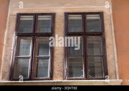 Two old wooden windows sit in a weathered stucco facade under warm daylight. Stock Photo