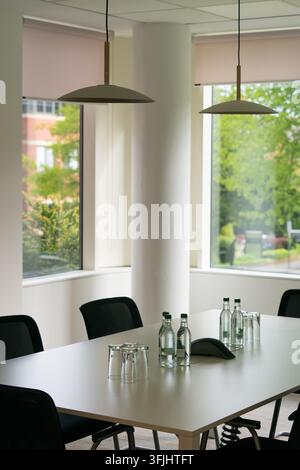 An empty conference table set with water and glasses inside a Regus shared office, prepared for a business meeting overlooking green trees. Stock Photo