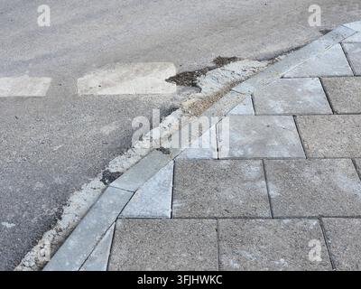 A close-up view of an urban street corner showing the junction between a paved sidewalk and an asphalt road. The right side and foreground feature a Stock Photo