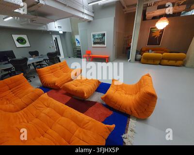 Modern office interior featuring vibrant orange modular lounge seating arranged on a colorful geometric area rug with blue, red, and orange patches. Stock Photo