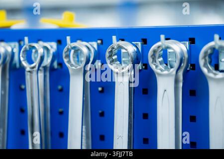 Ring spanners hang individually from hooks on a perforated tool board, displaying enclosed wrench heads used for gripping fasteners during mechanical Stock Photo