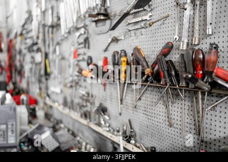 A neatly organized collection of hand tools including screwdrivers, wrenches, sockets and other equipment hanging on a pegboard wall in a professional workshop or garage. Stock Photo