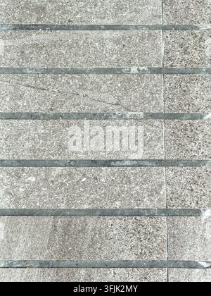 Top-down view of weathered rectangular pavement tiles arranged in a repeating geometric pattern with contrasting dark joints. Stock Photo