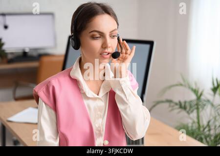 Customer support and remote assistance, young woman wearing headset working in office environment with computer and professional communication tools Stock Photo