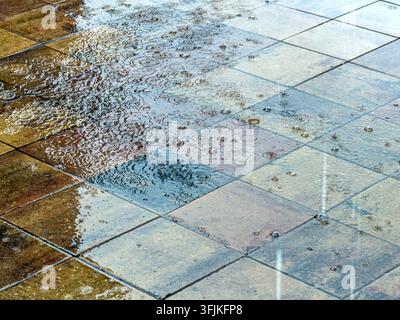 raindrops splashing on wet pavement tiles and creating ripples with bubbles. Stock Photo