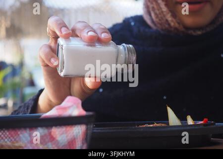 Person adding salt to food while sitting at a cafe in the outdoor area Stock Photo