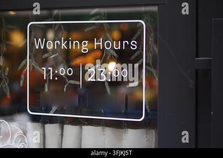 Working hours displayed on a business window in a busy area Stock Photo