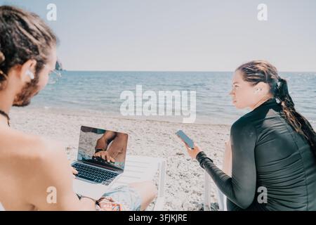 Beach Laptop Couple Working Remotely - Two people work on a laptop and phone on a beach. Stock Photo
