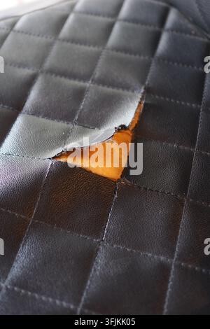 Torn black leather surface with visible orange material underneath Stock Photo