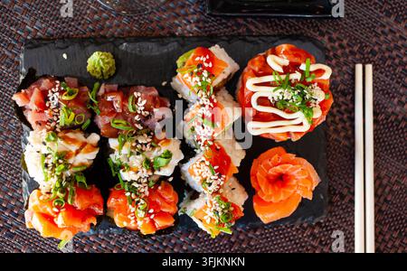 Traditional Japanese sushi platter. Gunkanmaki with various fillings, uramaki and raw salmon sashimi on slate serving board Stock Photo