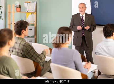Confident professor giving a lecture and using a clicker near monitor in classroom Stock Photo