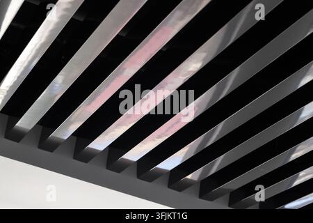 Modern interior featuring diagonal metal ceiling slats with reflective surfaces, strong geometric lines and repeating pattern. Minimal, industrial and Stock Photo