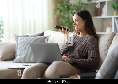 Young telecommuter using ai on phone to dictate prompt sitting on a couch at home Stock Photo