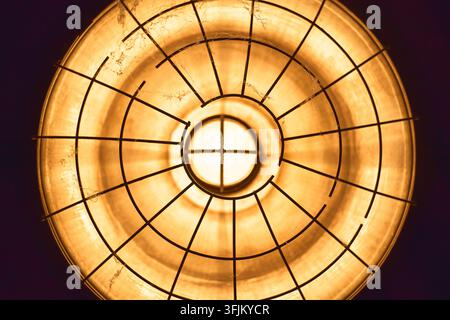 Industrial lamp creating a warm glow, illuminating darkness with radiating light and circular metal grid Stock Photo