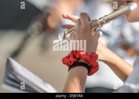 A close-up view of a person’s hands playing a silver flute outdoors, with blurred background and visible music sheets, capturing the focus and detail Stock Photo