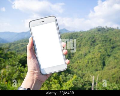 Mockup image of a hand holding and showing white smart phone with blank desktop screen in outdoor with blur green mountains background. Stock Photo