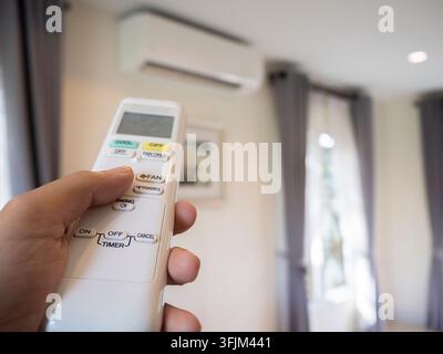 Woman's hand holding an air conditioner remote control to adjust the temperature in the house. Energy saving concept. Stock Photo