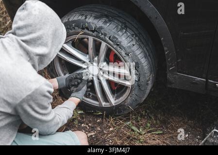 A young driver replaces the Blown Up flat Tire on his SUV car Stock Photo