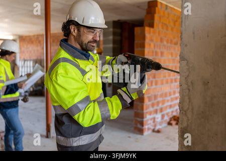 Professional builder using electric rotary hammer drill on concrete wall Stock Photo