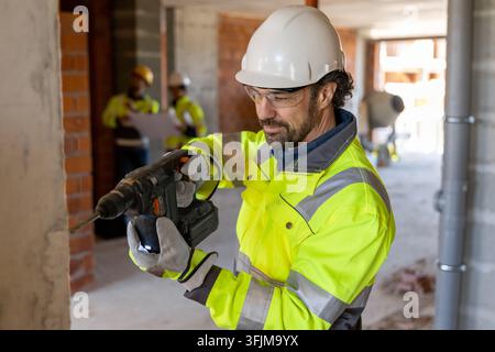 Focused builder using hammer drill on wall Stock Photo