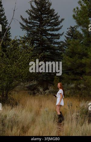 Woman with long red hair looks back in a forest clearing Stock Photo