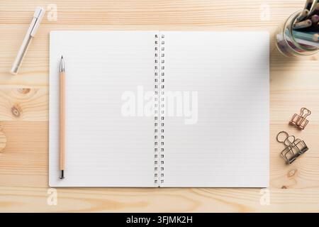 Top view of open lined spiral notebook mockup with stationery supplies on light wooden desk with copy space Stock Photo
