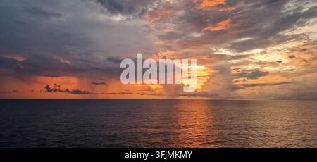Warm golden sunset breaking through dramatic clouds over the open ocean with sunlight reflected across the water. Stock Photo