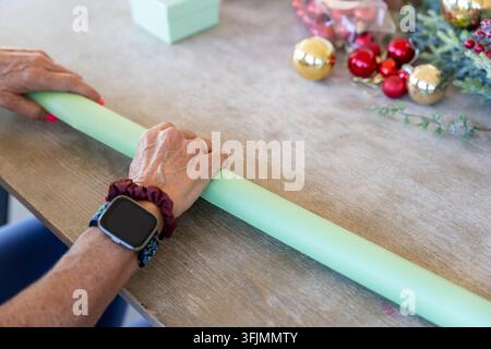 Hands unrolling mint green wrapping paper on a wooden table with christmas ornaments and gift boxes Stock Photo