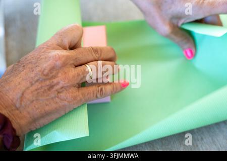 Hands wrapping a pink gift box with light green paper, preparing for celebration Stock Photo