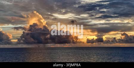 Dramatic towering clouds illuminated by warm evening sunlight over the open ocean. Stock Photo