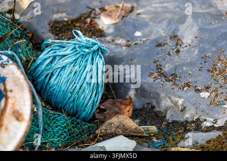 A roll of blue synthetic twine sits among plastic netting and garden debris on a clear plastic tarp. Natural daylight illuminates the texture of the d Stock Photo