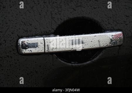 Close-up shot of a wet chrome car door handle with water droplets on a dark vehicle body after rain. Stock Photo